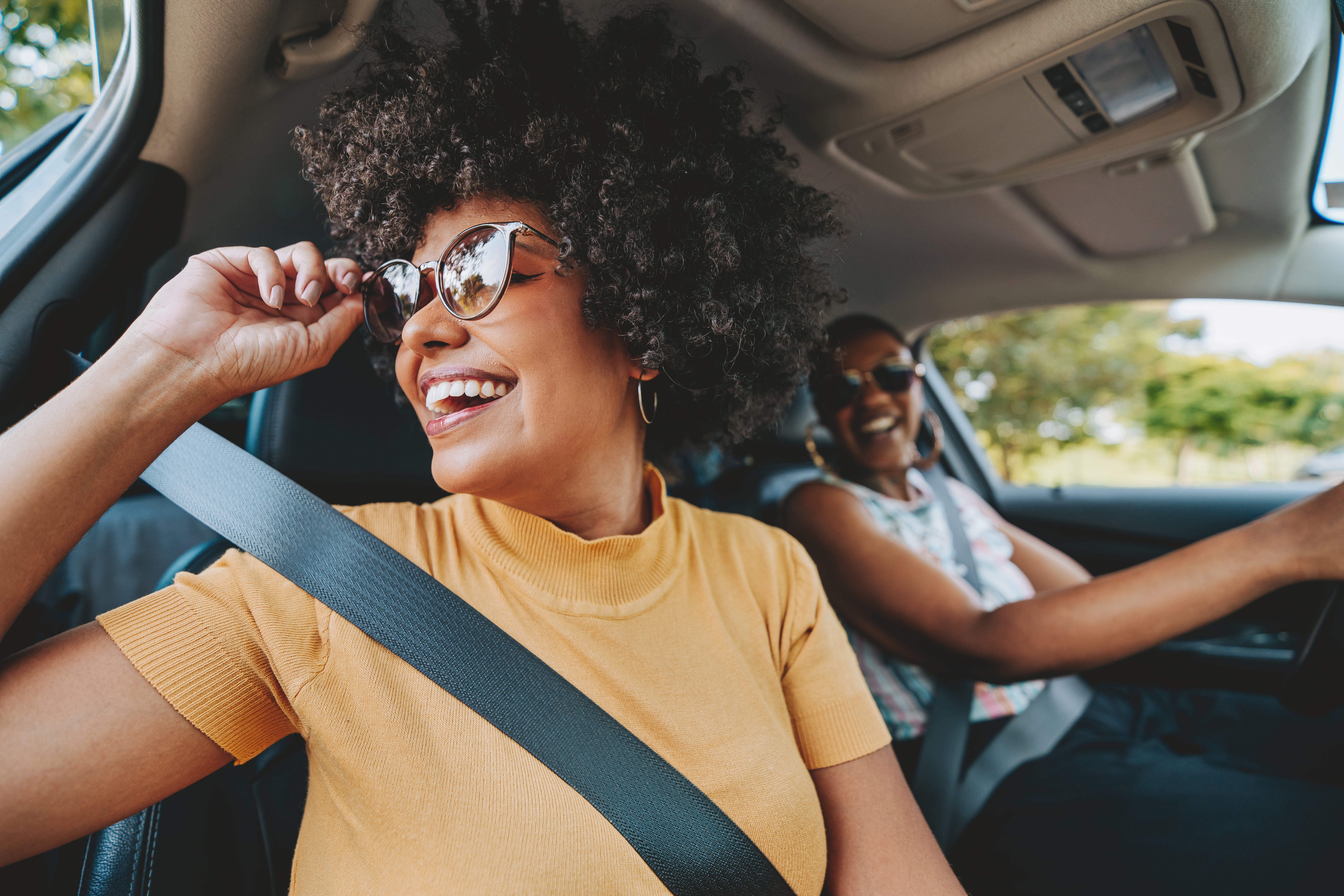 Two women wearing sunglasses and smiling in the car